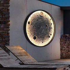 a circular light that is on the side of a building next to some rocks and logs