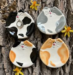 three cat shaped dishes sitting on top of a tree trunk with yellow flowers around them