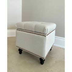 an upholstered foot stool with wheels and studding on the legs, against a white wall