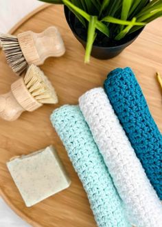 three crocheted washcloths sitting on top of a wooden table next to a potted plant