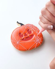 someone is decorating an orange cookie with white icing and spider webs on it