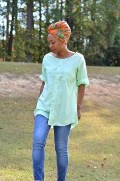 a woman standing in the grass wearing jeans and a green shirt with an orange head scarf