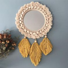 a round mirror with tassels hanging from it's sides next to dried flowers