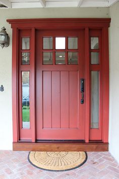 a red front door with two sidelights and a rug on the ground in front of it