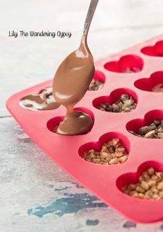 a spoon is pouring chocolate into a heart shaped muffin pan