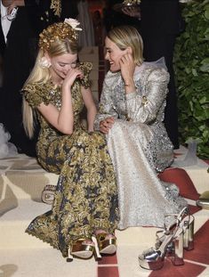 two women sitting next to each other on the ground in dresses and high heeled shoes