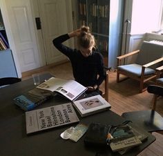 a woman sitting at a table with several books on top of it in front of a bookcase