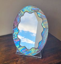 a mirror sitting on top of a wooden table next to a white wall and blue sky