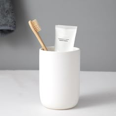 two toothbrushes in a white cup on a table