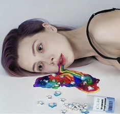 a woman laying on the ground next to an assortment of beads and paint tubes with her mouth open