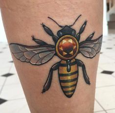 a bee tattoo on the leg with an orange and black circle in it's center