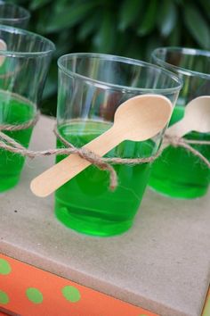 four glasses with green liquid and wooden spoons tied to each other on a table