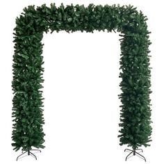 a tall green christmas tree next to a white wall with an arch made out of branches