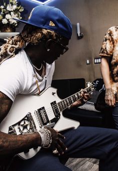 a man with dreadlocks plays an electric guitar in a room full of other people