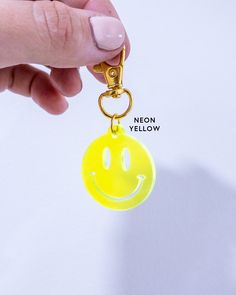 a hand holding a yellow smiley face keychain with the words neon yellow on it