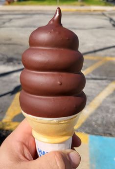 a hand holding an ice cream cone with chocolate on top in a parking lot area