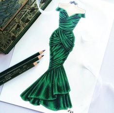 a drawing of a green dress on a piece of paper with two pencils next to it