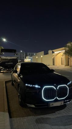 a black car parked on the side of a road next to a white truck at night