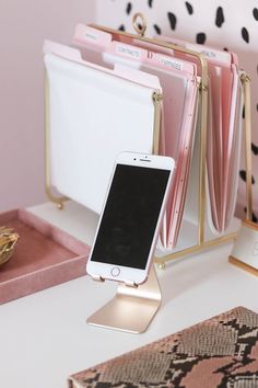 a cell phone is sitting on a stand next to some pink and gold accessories,