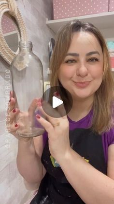 a woman holding a glass bottle in her hand and smiling at the camera while standing next to a shelf