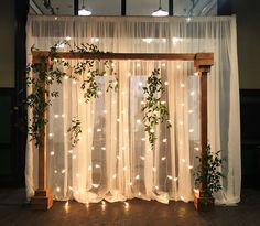 the curtain is decorated with greenery and lights for an indoor wedding ceremony or reception