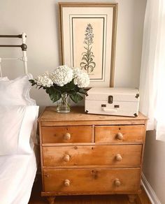 a dresser with flowers in a vase on top of it next to a white bed