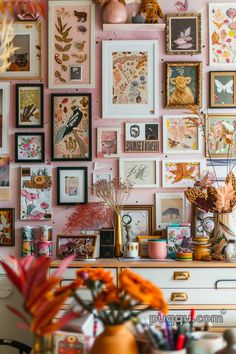 a wall full of framed pictures and flowers on top of a dresser next to a potted plant