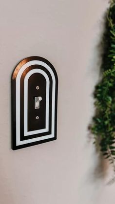 a black and white clock mounted to the side of a wall next to a green plant