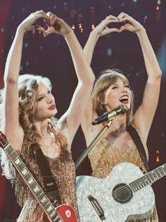 two women are performing on stage with their hands in the air and one is holding a guitar