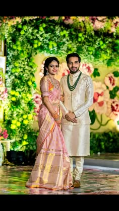 a man and woman standing next to each other in front of a flower covered wall