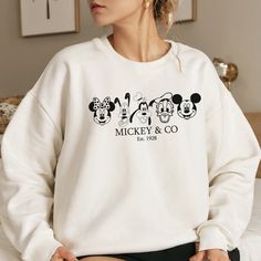 a woman sitting on top of a bed wearing a mickey mouse sweatshirt