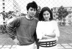 a man and woman standing next to each other in front of a chain link fence