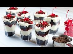 several desserts with cherries and whipped cream are arranged in individual cups on a tray