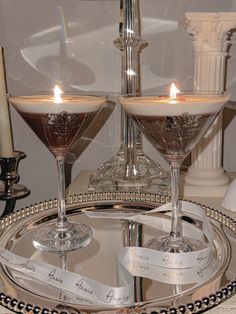 two martini glasses sitting on top of a silver tray next to each other with candles in them