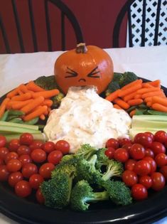 a black plate topped with carrots, broccoli and cauliflower next to a pumpkin