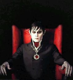 a man sitting in a red chair wearing a black suit