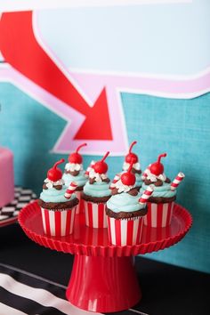 cupcakes with blue frosting and cherries are on a red cake stand