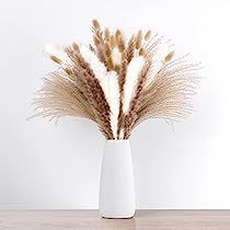 a white vase filled with dry grass on top of a wooden table