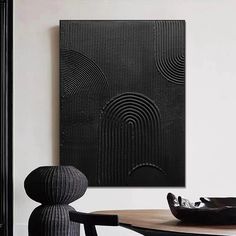 a table with a black vase on top of it next to a wall hanging art piece