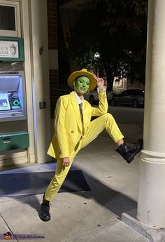 a man in a yellow suit and green face paint posing for a photo on the sidewalk