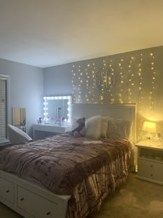 a bed room with a neatly made bed and lights on the wall above it's headboard