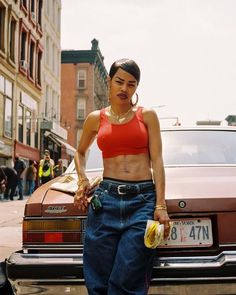 a woman standing in front of a car with her hands on her hip and holding bananas