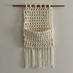 a white crocheted wall hanging on a wooden hanger with two tassels