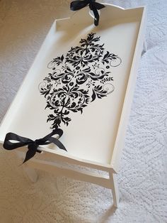 a white tray with black designs on it and a ribbon tied around the edge, sitting on a bed