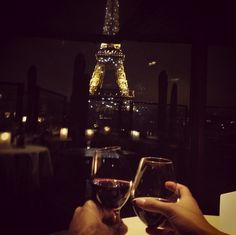 two people toasting wine glasses in front of the eiffel tower at night