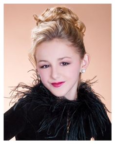 a young woman with blonde hair wearing a black jacket and posing for a photo in front of a beige background