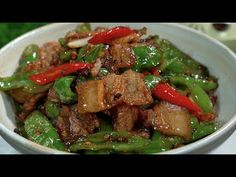 a white bowl filled with meat and green peppers on top of a table next to chopsticks