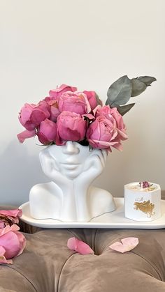 a white vase filled with pink flowers on top of a table