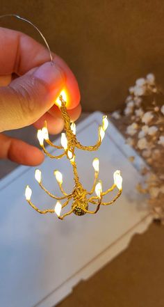 a hand holding a small gold chandelier with white lights