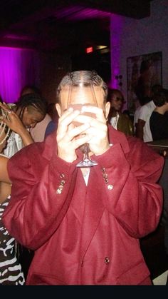 a man in a red jacket holding a wine glass up to his face while standing next to other people